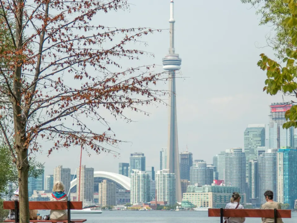 an image of the toronto skyline with people sitting on benches on Toronto Island contemplating moving to toronto.