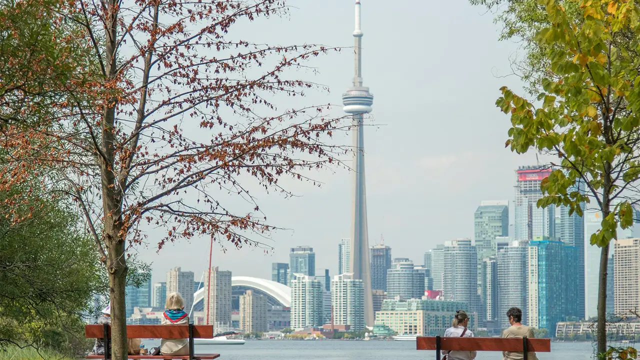 an image of the toronto skyline with people sitting on benches on Toronto Island contemplating moving to toronto.